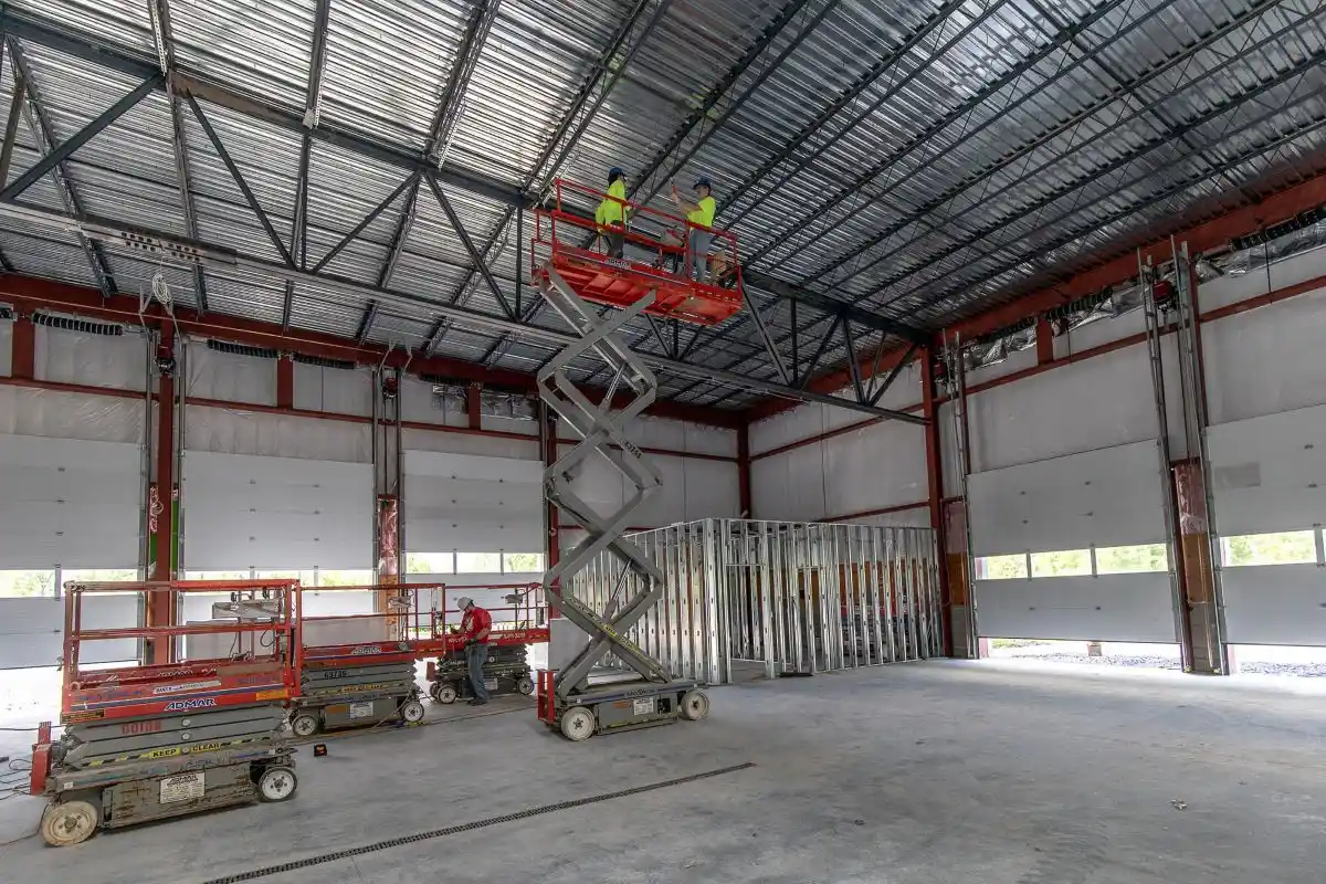 Commercial electricians installing and servicing overhead electrical systems inside a warehouse using lift equipment, supporting large-scale electrical installation and maintenance for a business facility.