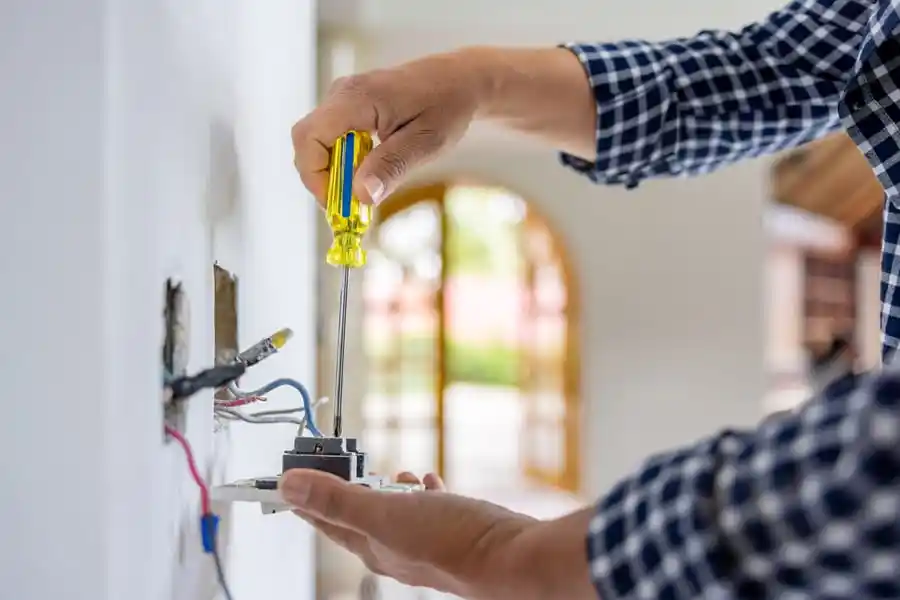 Electrician repairing and replacing a wall outlet by securing wiring and terminals to restore safe power and fix a faulty electrical connection in a residential home.